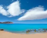 Traumhafter ibiza strand mit türkisblauem Wasser, goldenem Sand und einer felsigen Küste unter einem strahlend blauen Himmel mit weißen Wolken.
