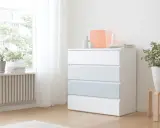 Eine weiße MALM Kommode mit vier Schubladen, eine davon hellblau, steht neben einem Fenster. Darauf sind Deko-Objekte und eine Kerze.
