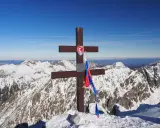 Drewniany krzyż z flagą Słowacji na szczycie Kriváň, narodowej góry Słowaków, na tle ośnieżonych Tatr.