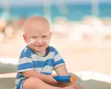 Un bébé souriant avec de la crème solaire sur le visage, tenant un tube de crème solaire. Idéal pour savoir crème solaire bébé à partir de quel âge.