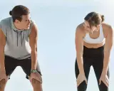 Zwei Läufer erholen sich nach einem anstrengenden 10 km Lauf. Sie schauen sich an, die Hände auf den Knien, erschöpft, aber zufrieden.