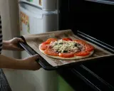 Wkładanie pizzy do piekarnika. Dzięki termoobiegowi ciasto będzie chrupiące, a ser idealnie roztopiony.
