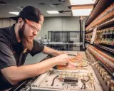Młody technik w okularach ochronnych pracuje nad skomplikowanym systemem przewodów, rozwijając swoje umiejętności w dziedzinie mechatroniki.