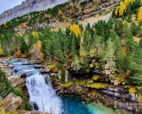 Cascada en un bosque otoñal de la cola de caballo huesca, con aguas turquesas y rocas cubiertas de musgo.