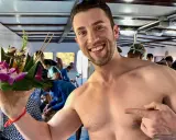 Smiling man on a boat in Asia, holding a flower offering. A perfect moment for gay travel in Asia.