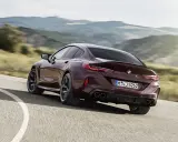 Ein dunkelroter BMW M8 Gran Coupé rast auf einer kurvigen Straße durch eine hügelige Landschaft.