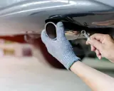 Ręka w rękawicy dokręca kluczem śrubę przy tłumiku końcowym samochodu.