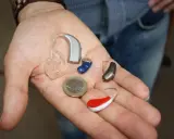 Na dłoni leżą aparaty słuchowe i moneta. Zastanawiasz się, ile kosztuje aparat słuchowy NFZ?