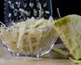 Frisch geriebener Apfel in einer Glasschale, daneben ein Apfelstück und eine Reibe.