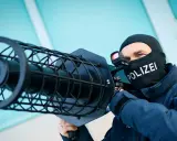 Polizist mit Sturmhaube und "POLIZEI"-Aufdruck zielt mit einer Drohnenabwehrwaffe.