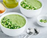 Deux bols de gaspacho concombre frais, garni de dés de concombre et d'herbes. Du pain grillé et de l'huile d'olive à proximité.