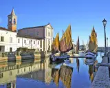 Barche a vela tradizionali ormeggiate sul canale di Cesenatico mare, con edifici storici e riflessi sull'acqua.