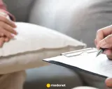 Dłoń pacjentki spoczywa na poduszce, podczas gdy psychiatra pisze zwolnienie od psychiatry na kartce.
