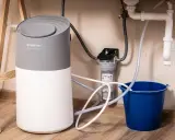 Instalación de descalcificador Equation bajo el fregadero, con filtro y cubo azul para recoger agua.