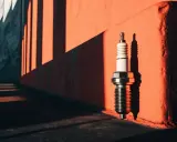 Une bougie d'allumage, comme une poire d'amorçage reste enfoncée, se dresse sur un mur orangé, projetant une ombre nette sous la lumière du soleil.