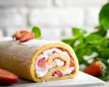 Delizioso rotolo panna e fragole, spolverato di zucchero a velo, con fragole fresche e menta sullo sfondo.