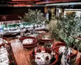 Elegant restaurang med runda, röda bås och träd. Köket syns i bakgrunden. Många gäster njuter av sin måltid. L'avventura recensioner verkar positiva.