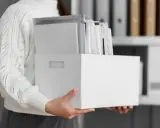 Osoba trzyma białe pudełko z dokumentami, ułatwiające przechowywanie dokumentacji pracowniczej.