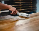 Main d'artisan appliquant une couche de vernis sur une table en bois avec un rouleau, pour la protéger et la sublimer.