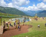 Un parco giochi in montagna con un laghetto, un galeone e tante famiglie che si divertono. Perfetto per le vacanze in montagna con bambini.