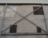 Estructura metálica en forma de X que refuerza una pared de concreto con ventanas de madera. La riostra, en este caso, es un elemento de soporte crucial.