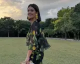 Isabelle Junot sonríe con un vestido estampado de limones, luciendo pendientes amarillos y un sombrero de paja en un día soleado.