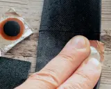 Łatka do dętki rowerowej z przerzutką w piaście. Dłoń przygotowuje łatkę do przyklejenia.