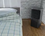 Un aire acondicionado portátil junto a una cama con sábanas a cuadros. ¿Qué es mejor, aire acondicionado portátil o fijo?