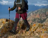 Osoba z plecakiem idzie po skalistym szlaku, używając kijków trekkingowych. Dobre kijki w góry to podstawa bezpiecznej wędrówki.