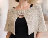 Mujer con un elegante **patrón capa** de ganchillo color beige, adornada con un broche floral.