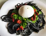 Czarny makaron z zielonym pesto, suszonymi pomidorami i kulką mozzarelli.