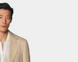 A man models a tan linen blazer over a white textured polo shirt, perfect for a smart casual dress code for a wedding.