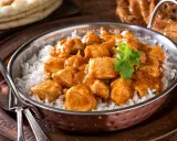 Un delicioso pollo al curry, un plato que evoca los sabores de la India, servido sobre arroz blanco en un cuenco de cobre.