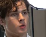 Młody mężczyzna z kręconymi włosami, jego twarz sugeruje wysoką skalę atrakcyjności mężczyzn.