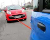 Czerwony Citroen holowany przez niebieski samochód. Pomarańczowa linka holownicza jest napięta, sugerując ruch i prędkość.