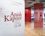 Biały plakat z napisem "Anish Kapoor" i czerwonymi rozpryskami na tle wystawy z czerwonymi zasłonami.