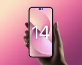 Dłoń trzyma różowy iPhone 14 z tapetą z cyfrą 14 na tle gradientu różu i beżu.