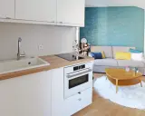 Aménagement petite cuisine moderne avec évier, plaque induction, four et salon cosy avec canapé bleu et jaune.