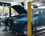 Taller mecánico con coches en reparación. Un todoterreno azul tiene el capó abierto, y se pregunta qué significa elevalunas.