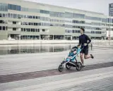 Ein Mann joggt mit Kinderwagen an einer modernen Fassade entlang. Das Kind schläft friedlich im Wagen.