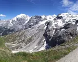 Panoramica mozzafiato dei fotografi sui tornanti dello Stelvio, con vette innevate e un cielo azzurro intenso.
