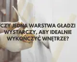 Ręce w rękawiczkach nakładają gładź na ścianę. Czy jedna warstwa wystarczy, by wykończyć wnętrze?