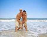 Two men laughing and embracing in the shallow waves of the Torremolinos gay beach.