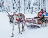 Familie im Rentierschlitten im verschneiten Wald, ein magischer Ausflug im Weihnachtsmann-Dorf Finnland.