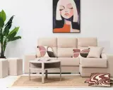 Sofá modular beige con chaise longue a la derecha, mesa auxiliar redonda, alfombra de yute, plantas y cuadro abstracto.
