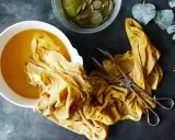 A yellow fabric is soaking in a bowl of golden liquid, part of a natural dye process. Eucalyptus leaves are nearby.