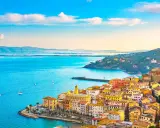 Colorate case affacciate sui mari della Toscana, con barche a vela che solcano le acque azzurre sotto un cielo limpido.