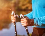 Radość z aktywnego życia po przeszczepie nerki. Dłonie trzymające kije do nordic walking na tle jesiennego krajobrazu.