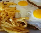 Un plato de milanesa a caballo argentina con papas fritas doradas y dos huevos fritos con yemas perfectas.
