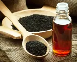 Huile de nigelle ambrée dans un flacon, à côté de graines noires dans une cuillère en bois. Découvrez les bienfaits de l'huile de nigelle.